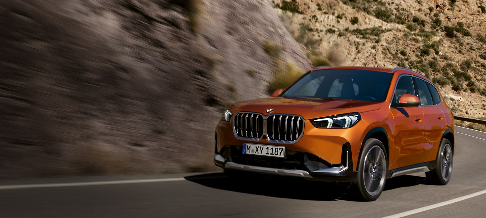 BMW X1 U11 xLine Utah orange metallic Dreiviertel-Frontansicht fahrend auf Landstraße