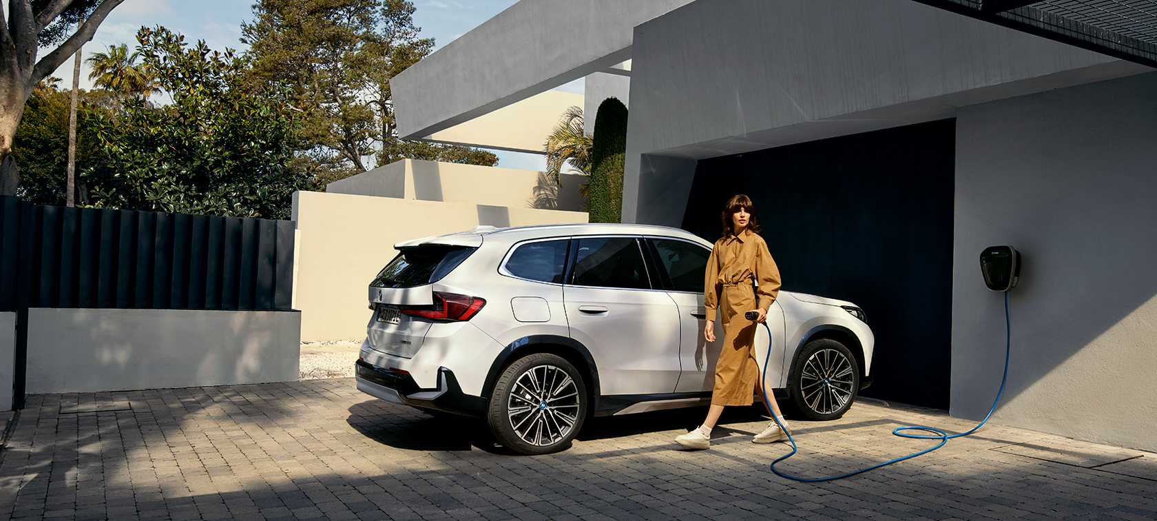 Eine Frau steht vor einem elektrischen BMW und sieht leicht zur Seite.